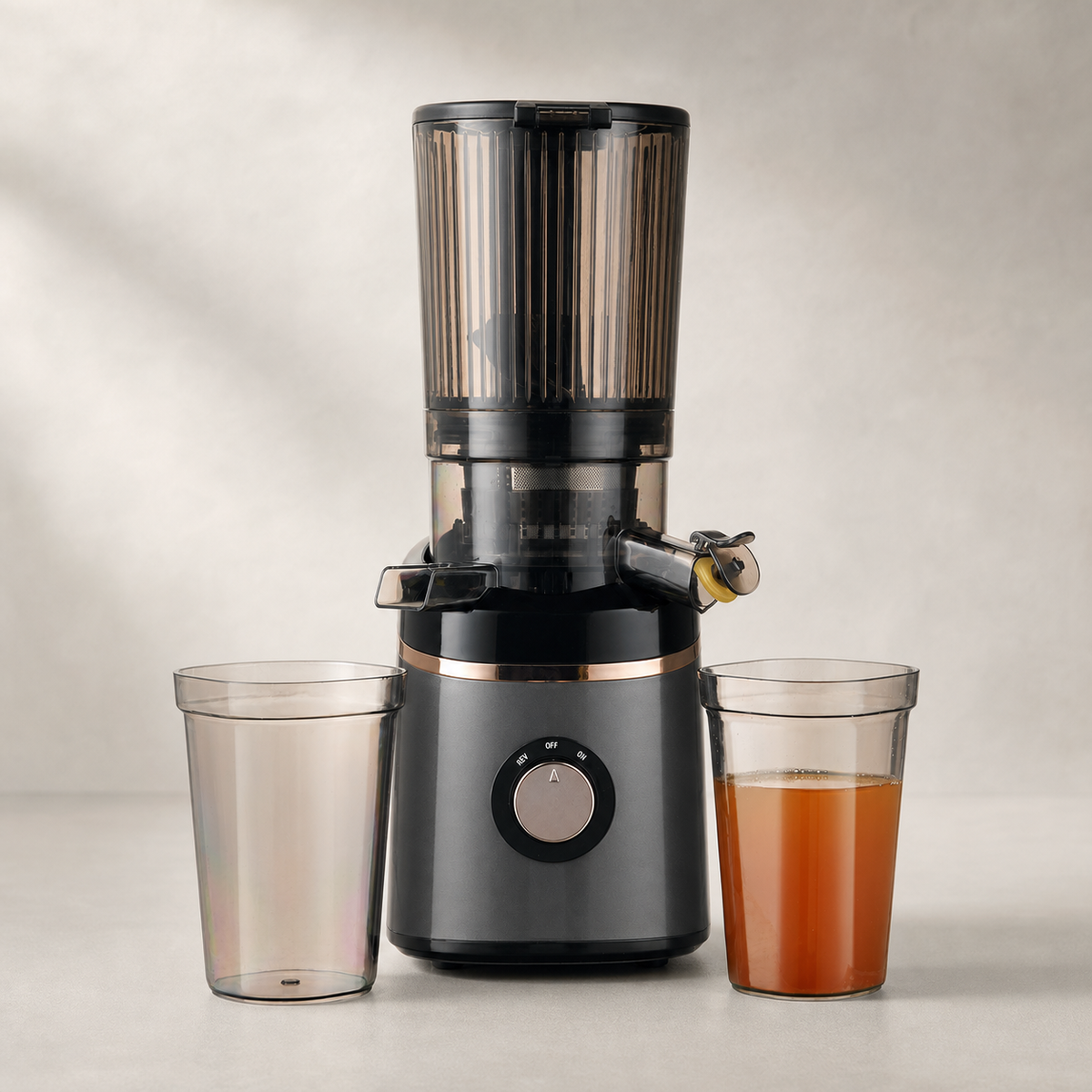 Graphite slow juicer with pulp and juice cups on a warm studio background